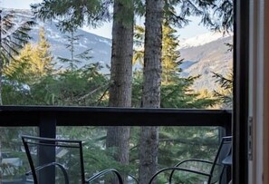 A balcony with two chairs, overlooking a forested area with tall trees and distant mountains.