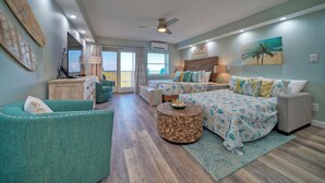 A spacious living room with a large bed, a green armchair, and a round coffee table. - 2 Beachfront Condos, Pool, Tennis/Pickleball, Gulf View | Island Retreat Complex (Port Aransas)
