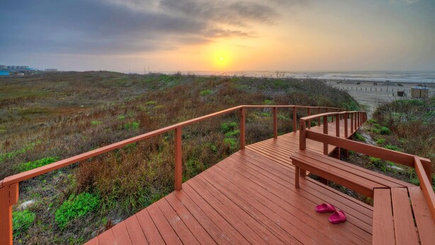 A wooden deck with a railing overlooking a beach and dunes during sunset. - 2 Beachfront Condos, Pool, Tennis/Pickleball, Gulf View | Island Retreat Complex (Port Aransas)