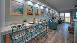 A modern kitchen with teal chairs, a dining table, and artwork on the walls. - 2 Beachfront Condos, Pool, Tennis/Pickleball, Gulf View | Island Retreat Complex (Port Aransas)