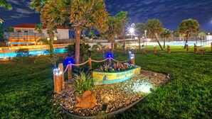 A nighttime view of a landscaped area with a sign for Farley Island Retreat II, surrounded by palm trees and a pool. - 2 Beachfront Condos, Pool, Tennis/Pickleball, Gulf View | Island Retreat Complex (Port Aransas)