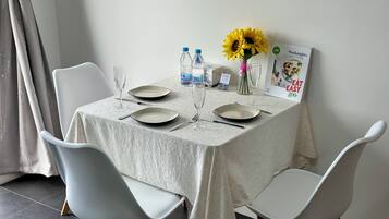 A dining table set with plates, cutlery, and glasses, surrounded by white chairs.