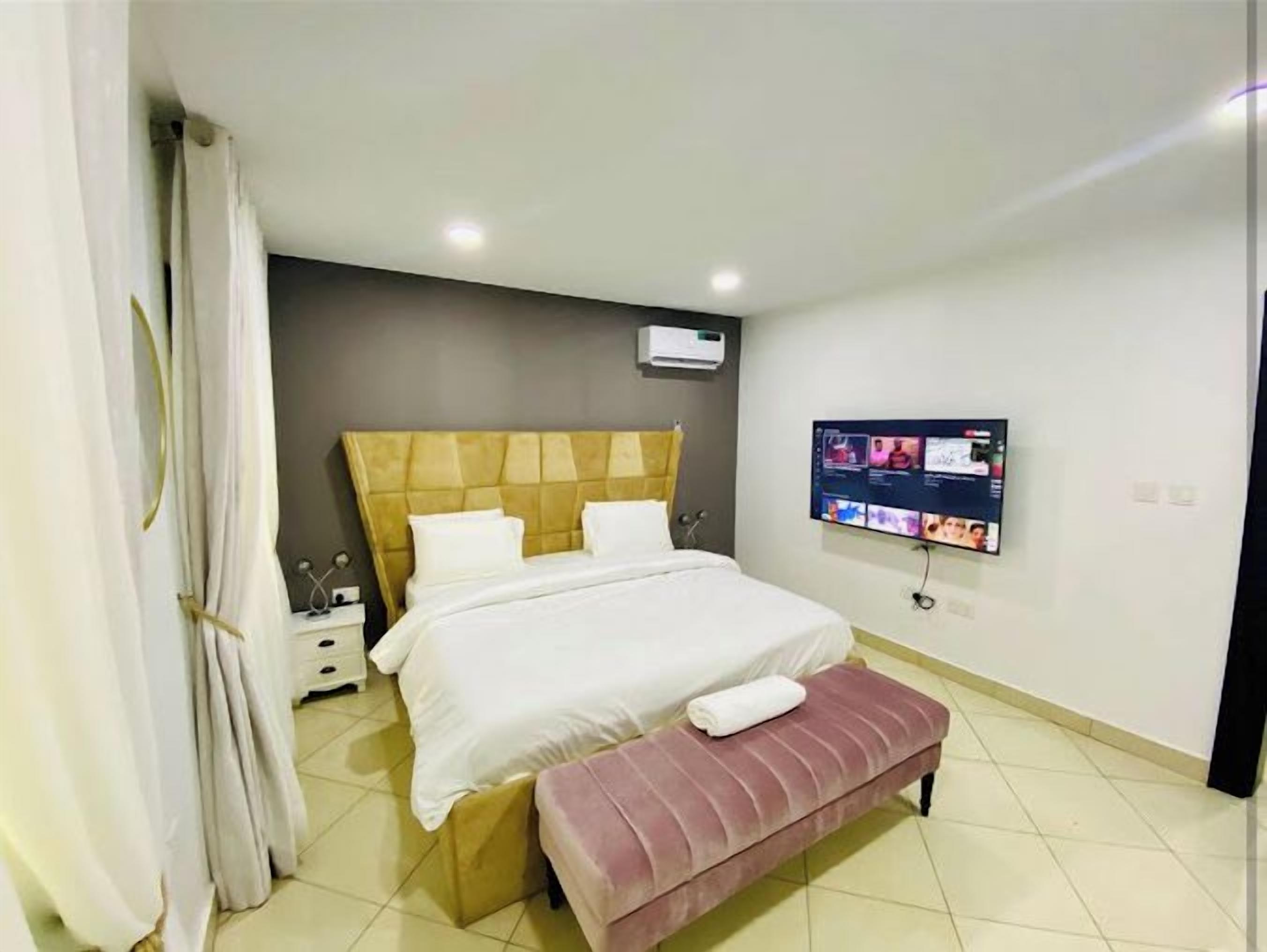 Ein modernes Hotelzimmer mit einem großen Bett, einem flachbildfernseher an der Wand, einem Nachttisch und einer Bank.