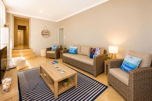 Una sala de estar con un sofá, dos sillones, una mesa de centro, un televisor y una lámpara.