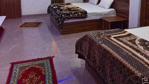 A hotel room with two beds, a wooden headboard, a ceiling fan, and a red decorative rug. - Hotel Sharda Palace (Vrindavan)