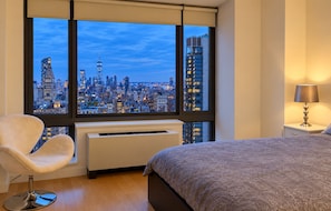 Ein Hotelzimmer mit großem Fenster, einem Bett, einem Sessel, einem Nachttisch mit Lampe und einem Wandheizgerät.