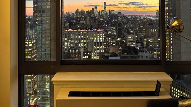 Quarto com uma grande janela com vista para a paisagem urbana ao entardecer.