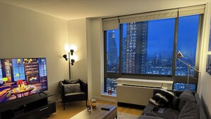 Uma sala de estar moderna com televisão, sofá, mesa de centro e uma janela grande com vista para a cidade.