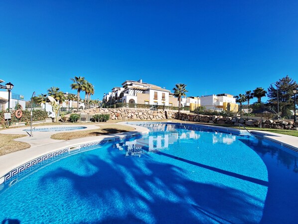 Relax by the resort's serene pool surrounded by lush greenery and Mediterranean-style buildings.
