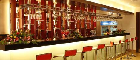 A bar area with a long counter, multiple stools, and a variety of bottles and glasses on shelves.