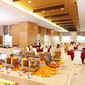 A banquet hall with round tables, buffet stations, and a person in the background. - Majestic Mong Cai Hotel (Mong Cai)
