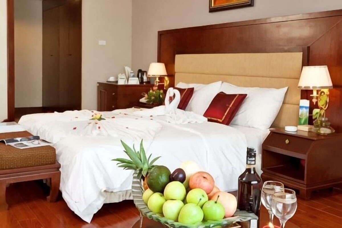 A hotel room with a large bed, bedside tables, a fruit bowl, and a nightstand with a lamp.