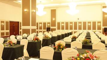 A banquet hall with rows of tables, each with a water bottle, a glass, and a flower centerpiece.