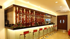 Uma área de bar com balcão, banquetas e uma exposição de copos.
