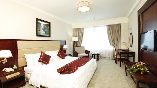 Quarto de hotel com uma cama grande, mesas de cabeceira, uma escrivaninha, uma cadeira, uma televisão e um quadro na parede.