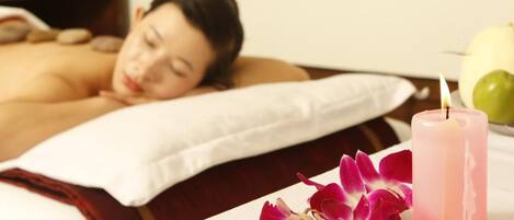 A person lying on a bed in a room with a white pillow, a pink candle, and a flower on the bedside table.