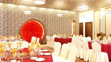 A banquet hall with round tables, white chairs, and red tablecloths.