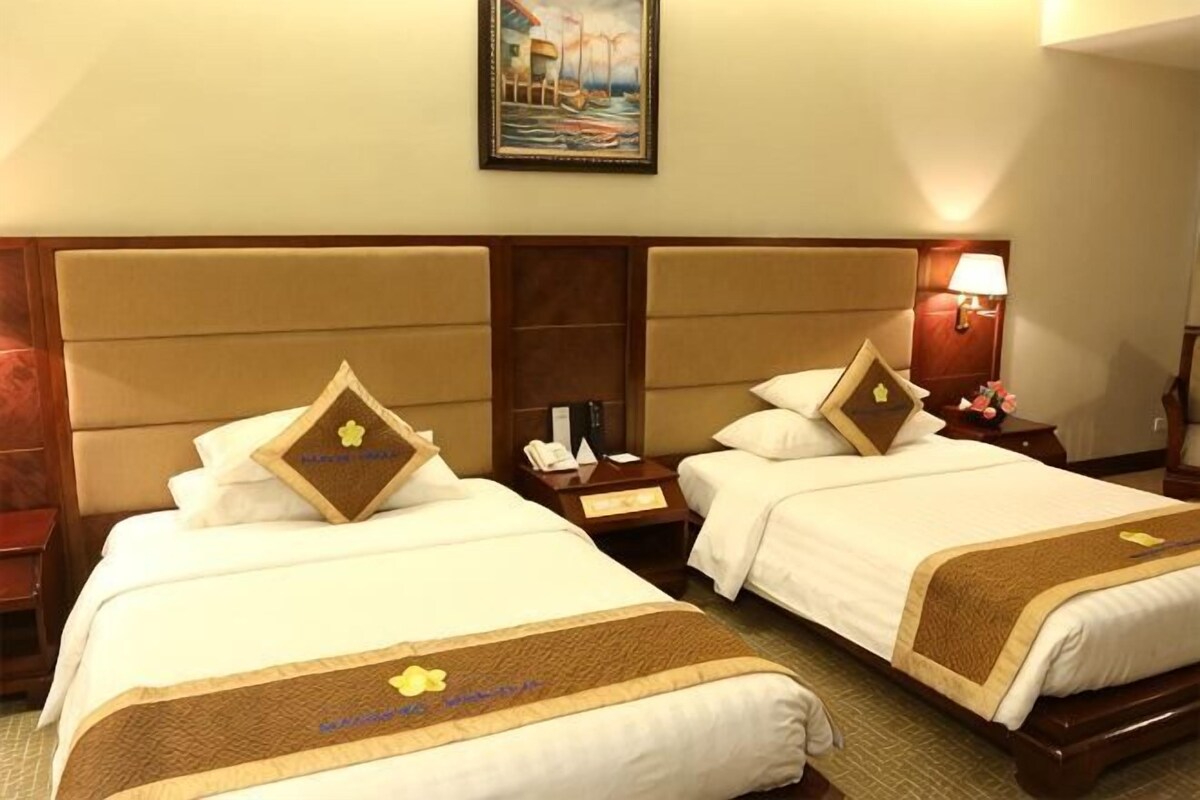 A hotel room with two beds, each with a headboard, a nightstand, a lamp, and a framed picture on the wall.