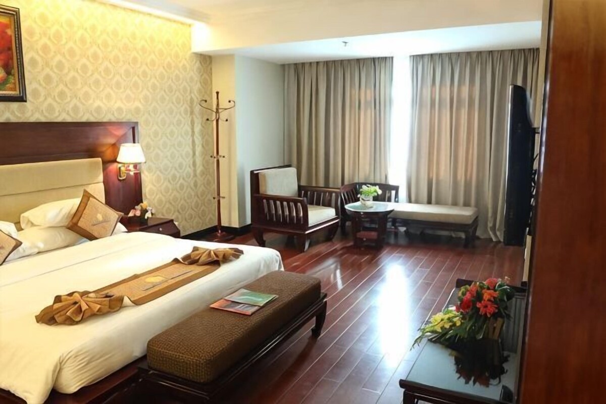 A hotel room with a large bed, a desk, a chair, a television, and a window with curtains.