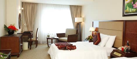 A hotel room with two beds, a desk, a chair, a lamp, and a painting on the wall.