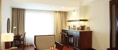 Habitación de hotel con comedor, bar y un amplio ventanal con cortinas.