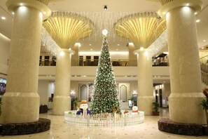 A lobby with a large Christmas tree, columns, and a white fence. - Majestic Mong Cai Hotel (Mong Cai)