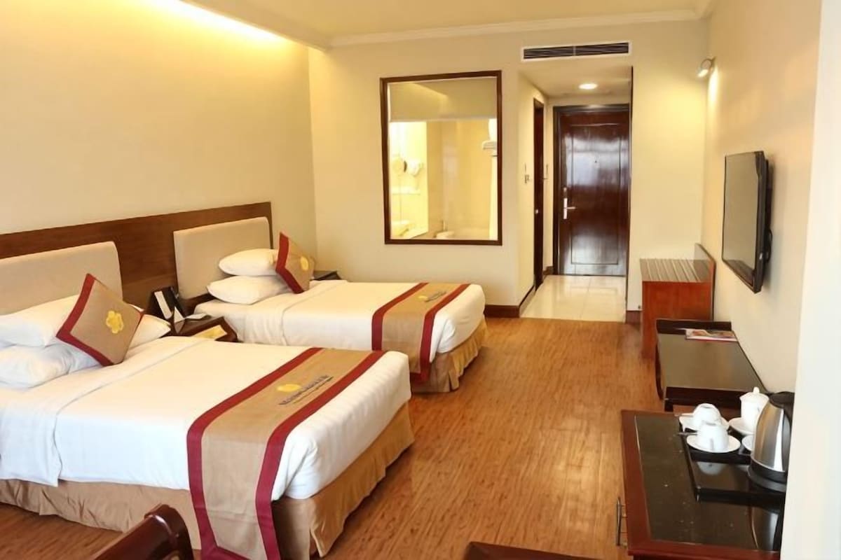 A hotel room with two beds, a desk, a chair, a TV, and a mirror.
