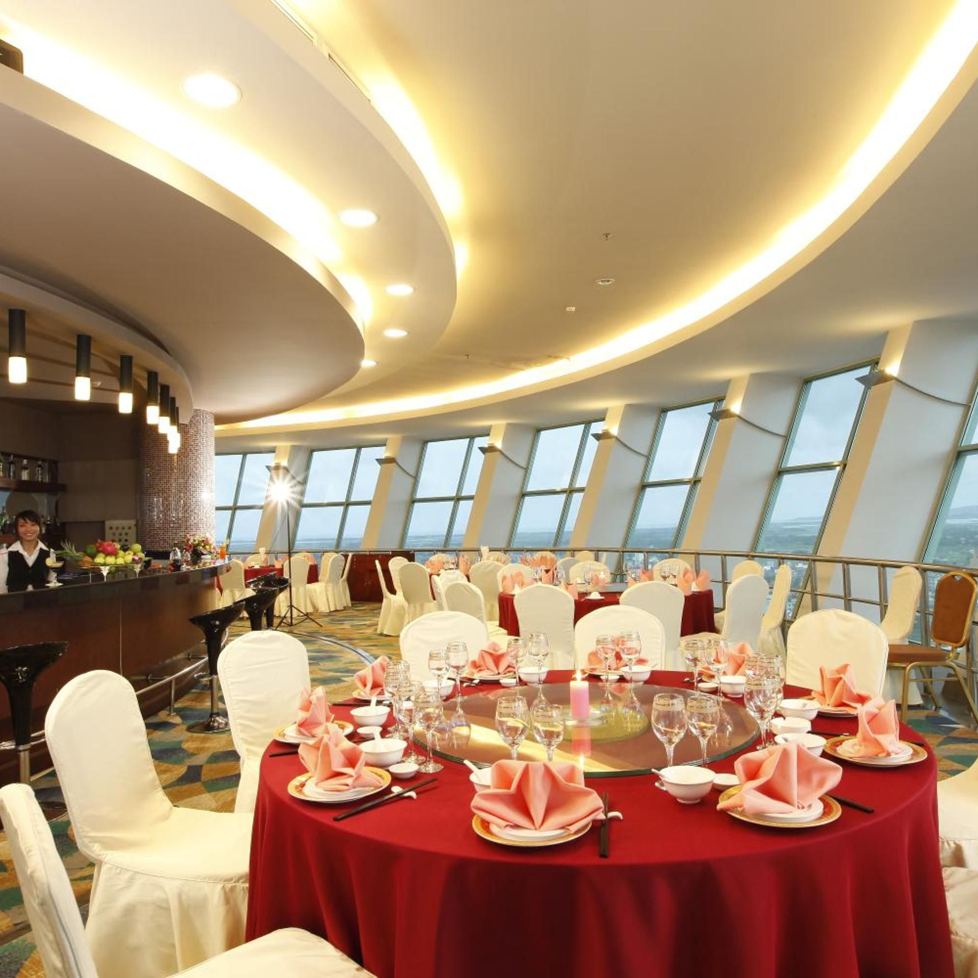 A formal dining area with round tables, white chairs, and red tablecloths.