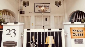 A hotel entrance with a white facade, numbered doors, and a sign for 'KYASH CUBES'. - Georgetown Kyash House 23 (Northeast Penang Island)