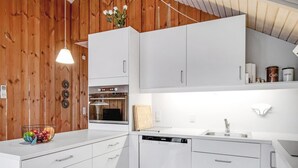 Une cuisine moderne avec des meubles blancs, un four encastré, un lave-vaisselle et un lambris mural en bois.