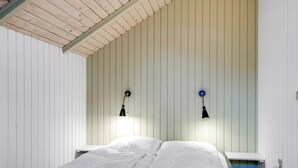 Une chambre avec un plafond en bois, deux lampes de chevet, un lit avec une literie blanche et un mur d’accent bleu.