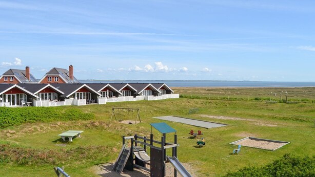 Une rangée de charmantes maisons aux toits rouges et aux balustrades blanches, une aire de jeux et un champ verdoyant offrant une vue sur la mer.