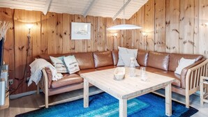 Une pièce chaleureuse avec un décor intérieur en bois, un canapé en cuir marron, une table basse en bois et un tapis bleu.