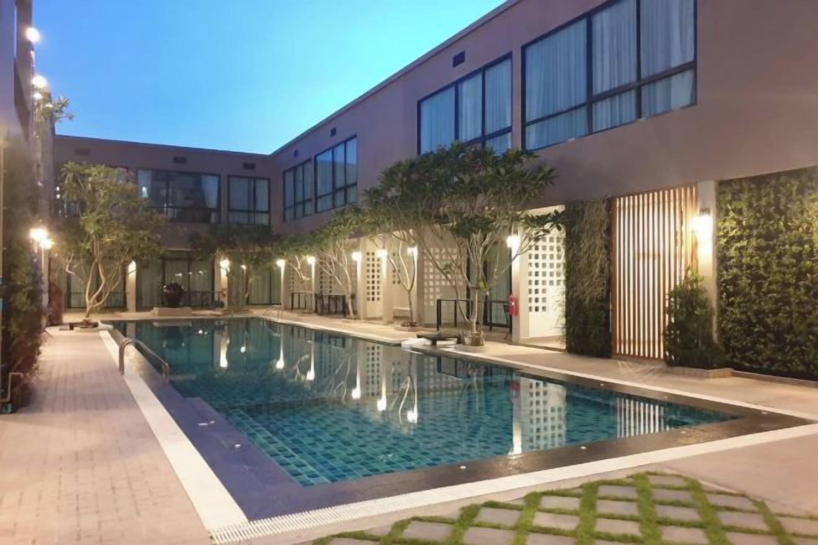Una piscina con solárium de azulejos, rodeada por un edificio con grandes ventanales y techo plano.