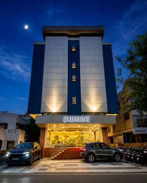 Un hotel llamado 'President', con un diseño moderno, que presenta una entrada destacada y un estacionamiento con coches.