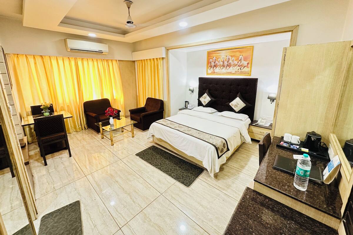 Une chambre d’hôtel avec un lit, deux fauteuils, une petite table avec un vase, un bureau avec un téléphone et un tableau au mur.
