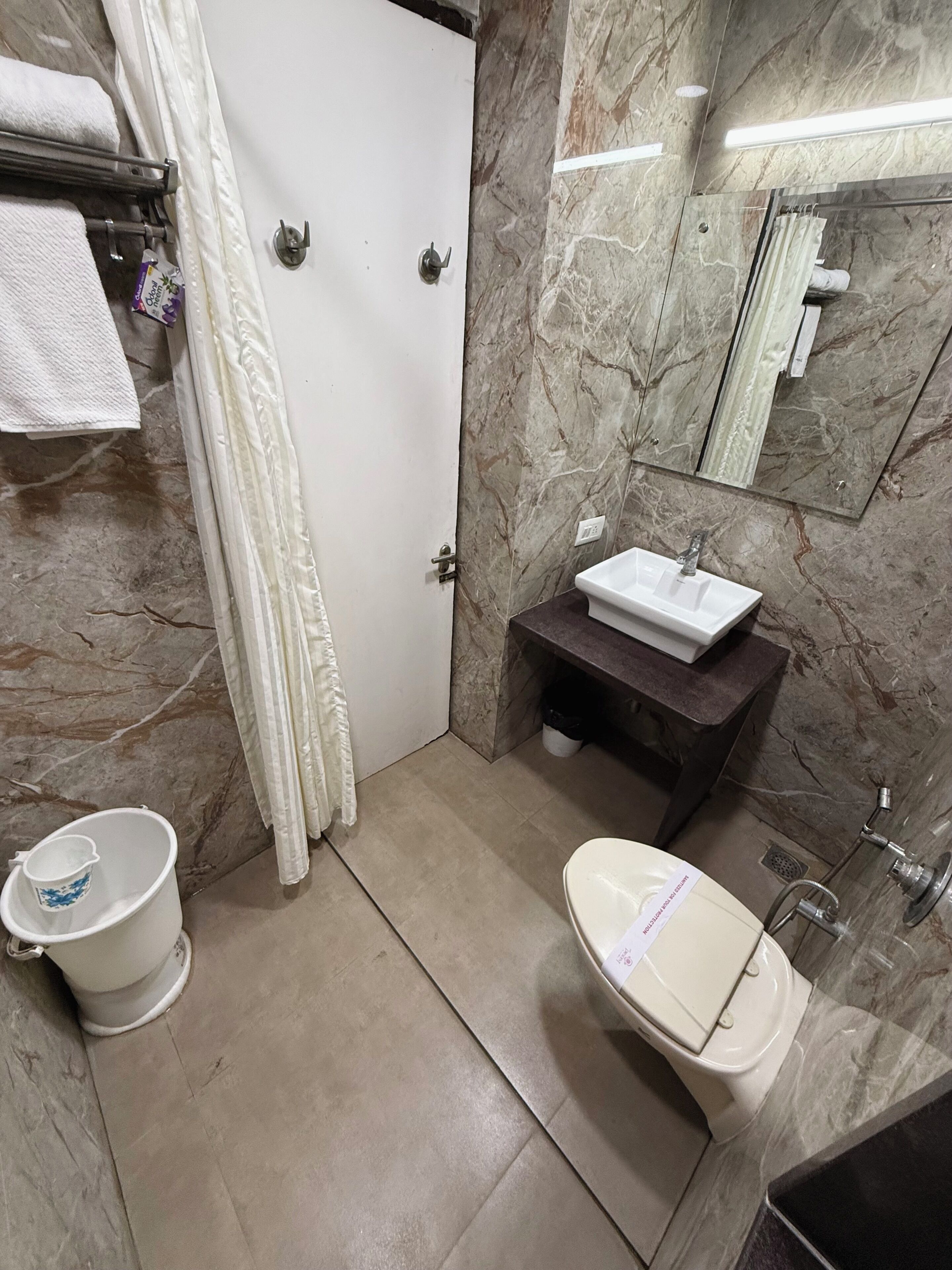 A bathroom with a white sink, a toilet, a shower, and a marble wall.