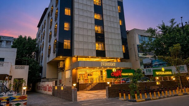 Un hotel de varios pisos con un diseño moderno, que presenta una entrada destacada y señalización para 'President' y 'Punjab Taste'.