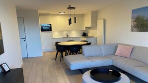 A modern living room with a grey sofa, a round coffee table, and a dining area with a table and chairs.