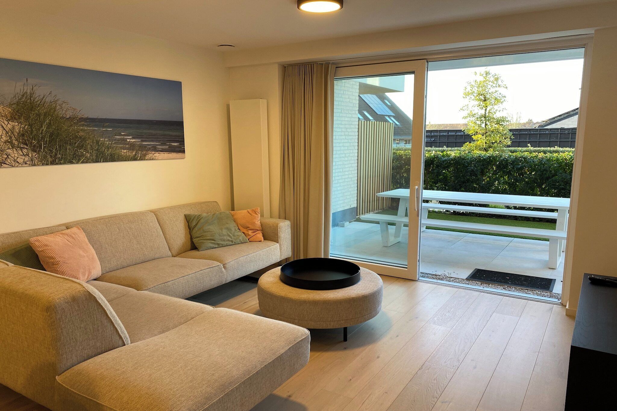 A modern living room with a sofa, a coffee table, and a large window with a view of a garden and a building.