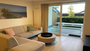 A modern living room with a sofa, a coffee table, and a large window with a view of a garden and a building.