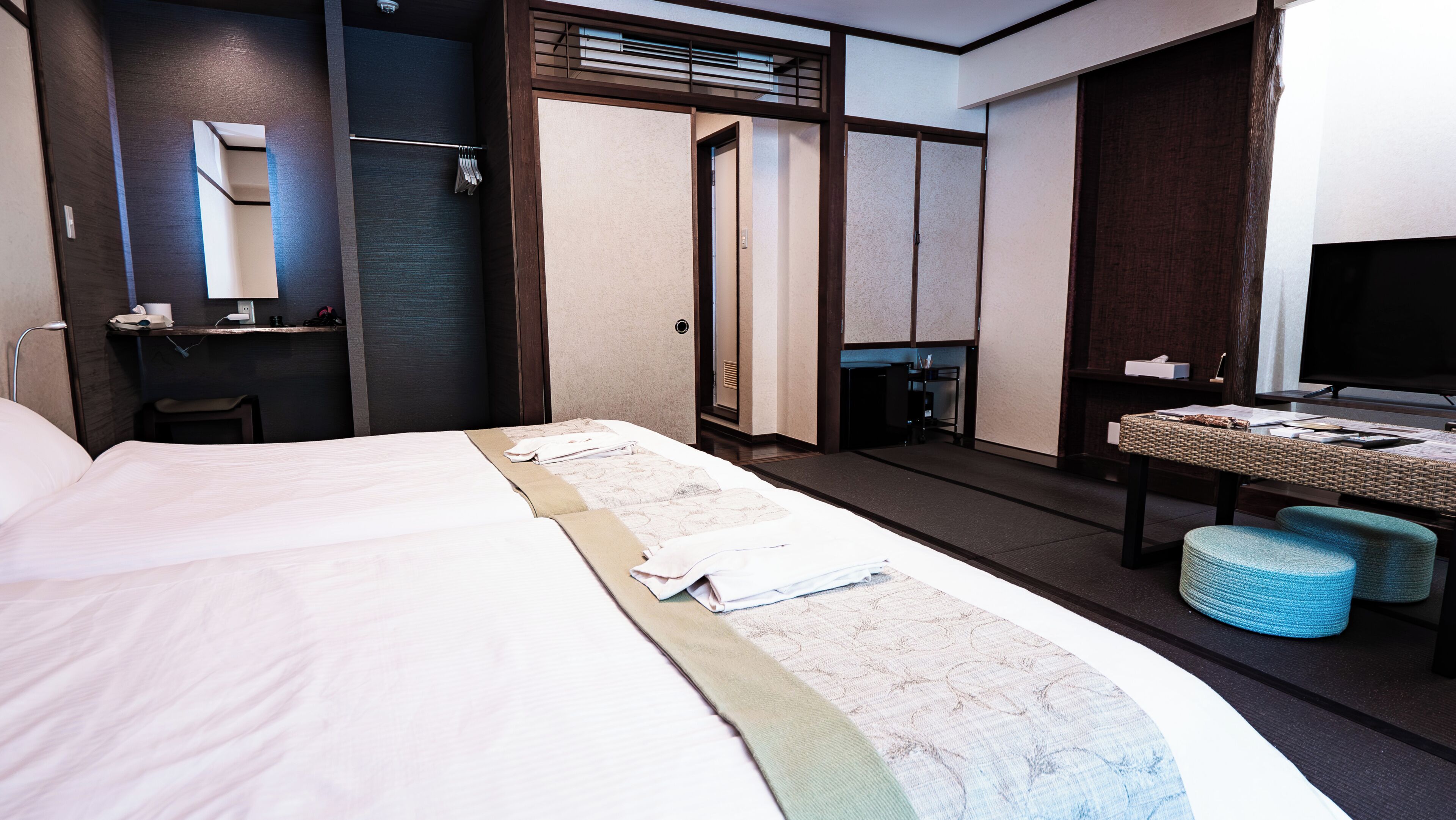 Una camera d'albergo con un letto grande, una scrivania con una sedia, una televisione e un bagno con uno specchio e un portaserviti.