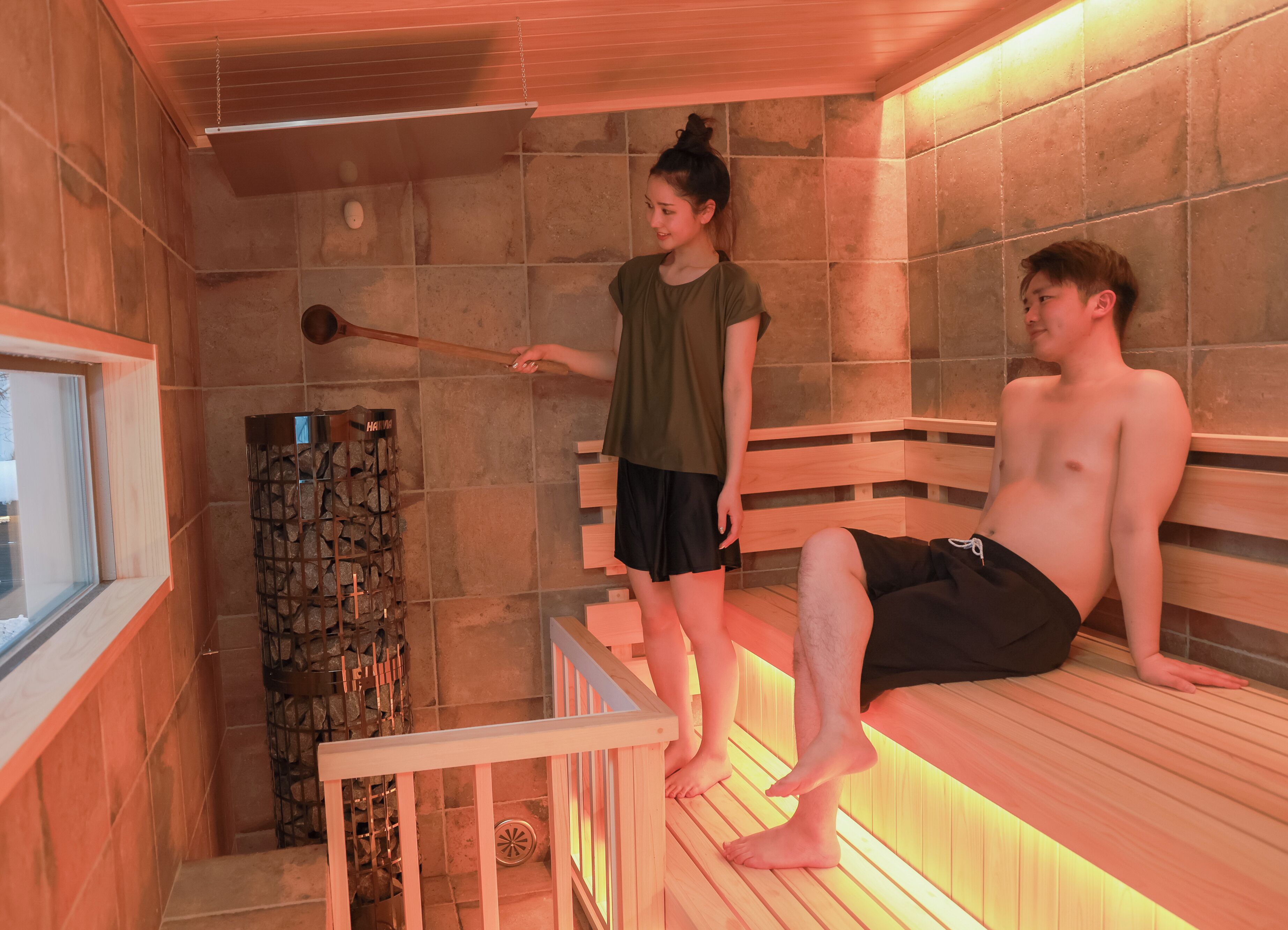 A sauna room with a wooden bench, a stone wall, and a wooden door.
