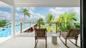 A balcony with two wicker chairs, a small round table, and a view of a swimming pool and palm trees. - King’s Crown – Luxury Waterfront Estate on Harbour Island, Bahamas (Dunmore Town)