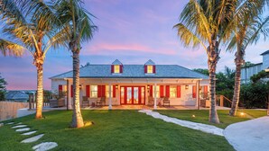 A two-story house with a red door and windows, surrounded by a well-maintained lawn and palm trees. - King’s Crown – Luxury Waterfront Estate on Harbour Island, Bahamas (Dunmore Town)