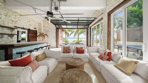 A spacious living area with white sofas, a pool table, and large windows offering a view of the ocean. - King’s Crown – Luxury Waterfront Estate on Harbour Island, Bahamas (Dunmore Town)