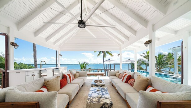 A covered outdoor seating area with white furniture, a marble coffee table, and a view of the ocean. - King’s Crown – Luxury Waterfront Estate on Harbour Island, Bahamas (Dunmore Town)