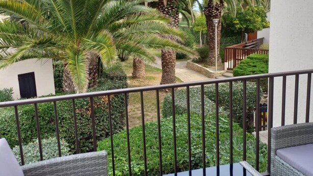 A balcony with wicker furniture and a view of palm trees and a garden. - Joli studio face à la mer avec accès direct (Saint-Cyprien)