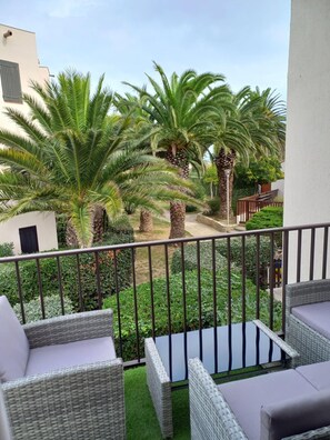 Een balkon met rieten meubilair en uitzicht op palmbomen en een tuin.
