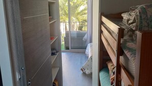 A narrow room with a wooden wardrobe, a bunk bed, and a sliding glass door leading to a balcony with a view of palm trees. - Joli studio face à la mer avec accès direct (Saint-Cyprien)